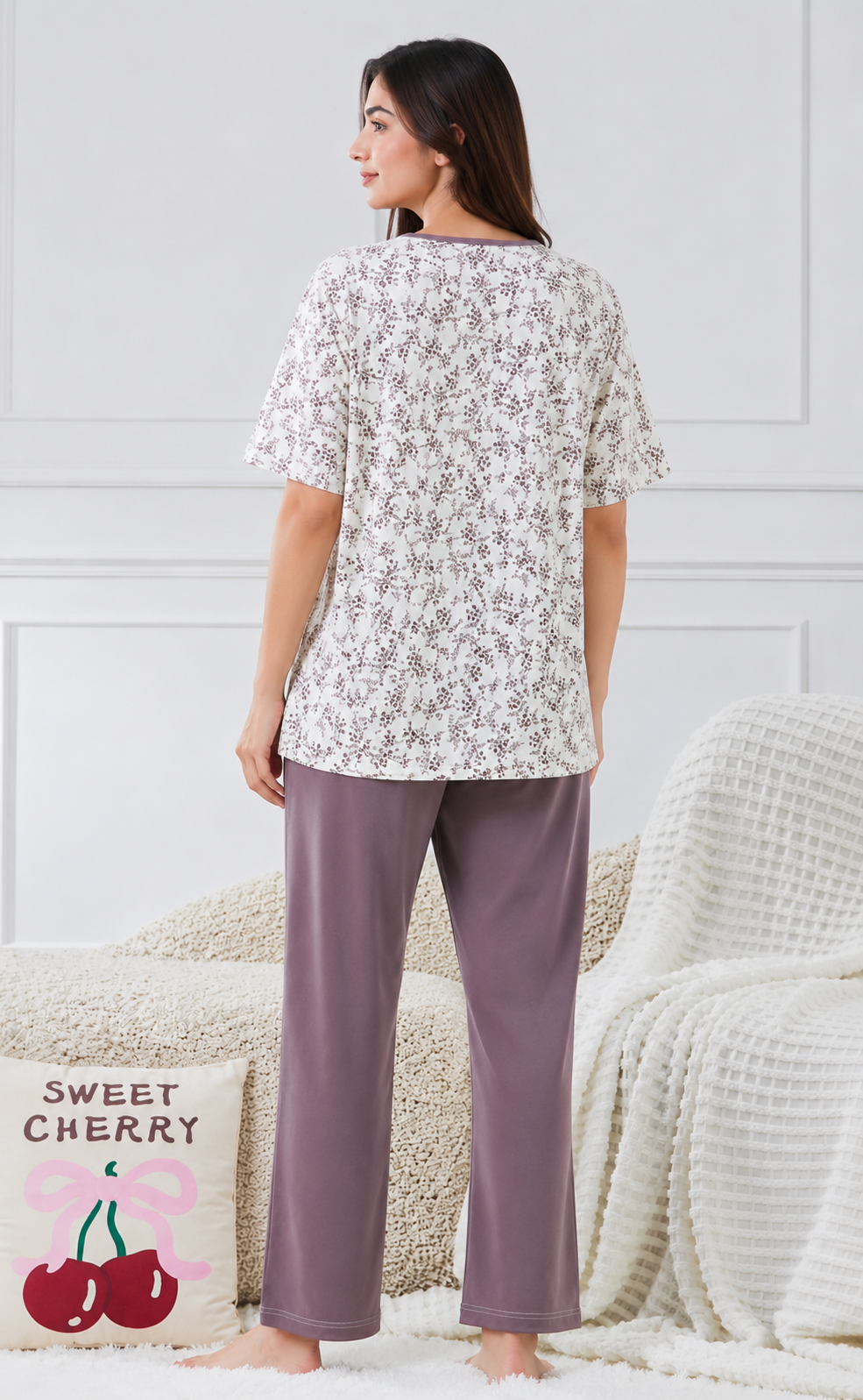 Woman wearing a floral top and purple pants in a cozy room.