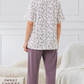 Woman wearing a floral top and purple pants in a cozy room.

