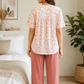 Woman wearing a pink lace top and pants in a bedroom setting.

