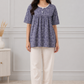 Woman wearing a blue floral top and white pants in a room with a neutral background

